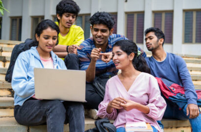 Group of happy students checking results on laptop while sitting on college campus - concept of education, technology and project work discussion